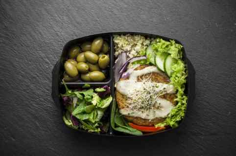 Vorratsdose mit drei Fächern. Darin: Oliven, Salat und ein Gemüseburger mit Salatbeilage.