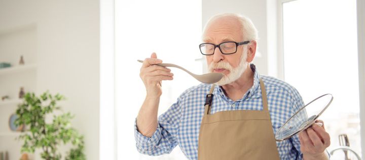 Bild: Ein älterer Mann kocht und schmeckt ab.