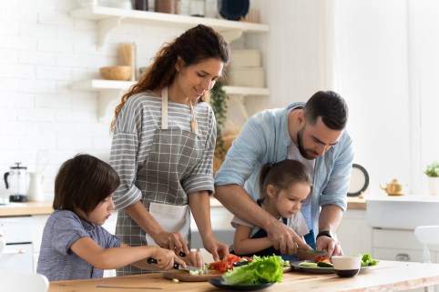 Eine junge Familie schneidet zu viert Gemüse in der Küche