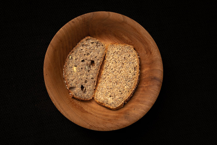 Zwei Scheiben Brot liegen nebeneinander in einer Holzschale: eines feucht und großporig, eines mit gleichmäßiger Krume.