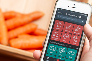 Handy mit Einkaufslisten-App vor einer Kiste Karotten.