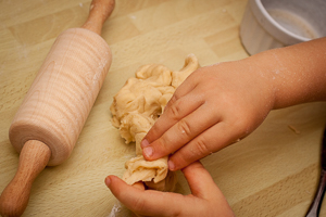 Kinderhände bearbeiten eine Portion Hefeteig. Daneben liegt ein Kinder-Nudelholz.