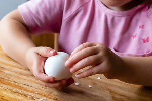 Kinderhände schälen ein weißes Ei.