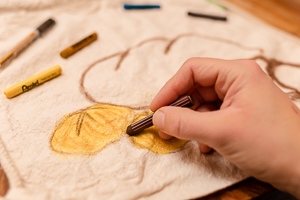 Erwachsenenhand malt Brot und Brötchen auf einen Leinenbeutel.