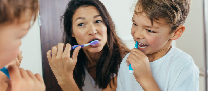 Mutter und Sohn putzen gemeinsam vor dem Spiegel ihre Zähne.