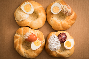 Eiervergleich: Vier gebackene Osterkränze, darauf jeweils ein aufgeschnittenes Ei.
