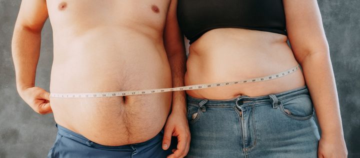 Ein übergewichtiges Paar steht nebeneinander und messen ihrem BMI mit einem Massband