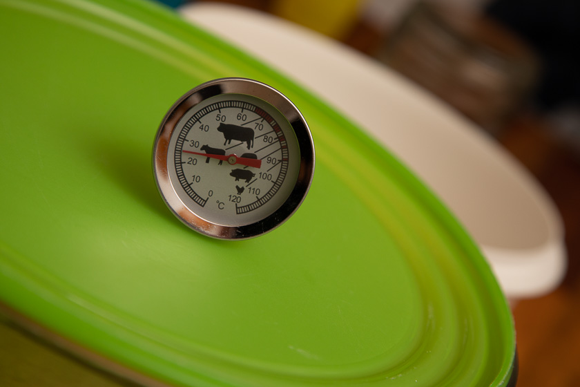 Lebensmittelthermometer liegt auf dem grünen Deckel einer Schüssel. Der Zeiger ruht auf 25 Grad Celsius.