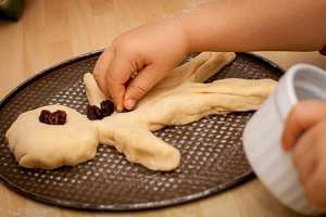 Kinderhand drückt Rosinen in einen Weckmann-Rohling.