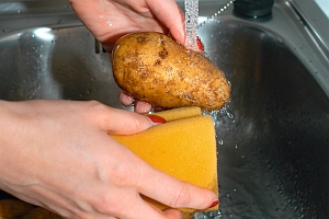 Hände halten Kartoffel unter Wasserhahn und Schwamm