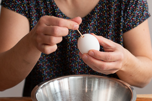 Frauenhand sticht mit Zahnstocher in ein Ei.