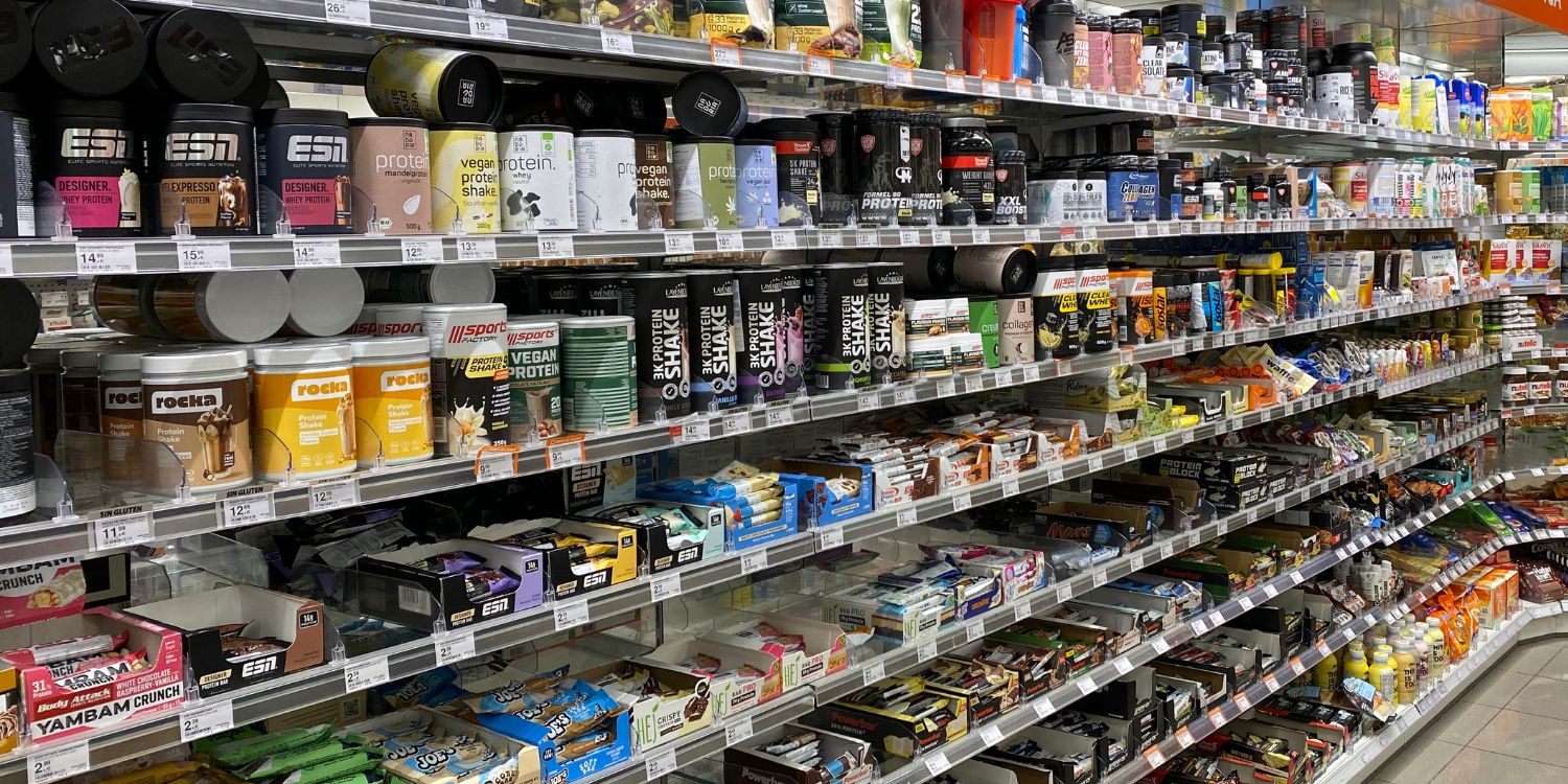 Ein Regal in einem Supermarkt ist gefüllt mit Proteinriegeln und Proteinpulvern. . Artikel "Proteine im Spiegel von Gesellschaft und Forschung " öffnen.