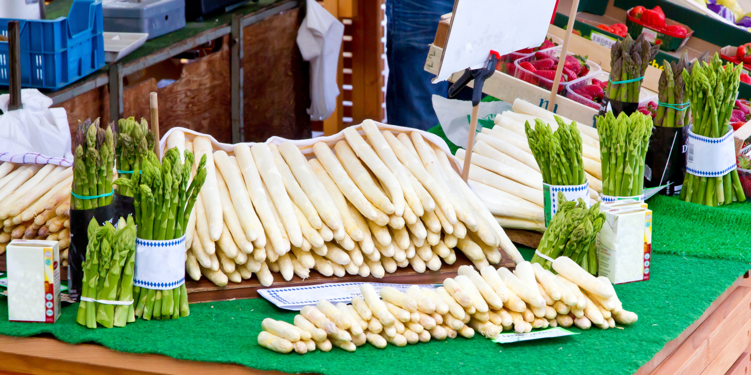 Grüner und weißer Spargel liegen in der Auslage eines Marktstandes.. Artikel "Spargel: Von der Ernte in den Handel" öffnen.
