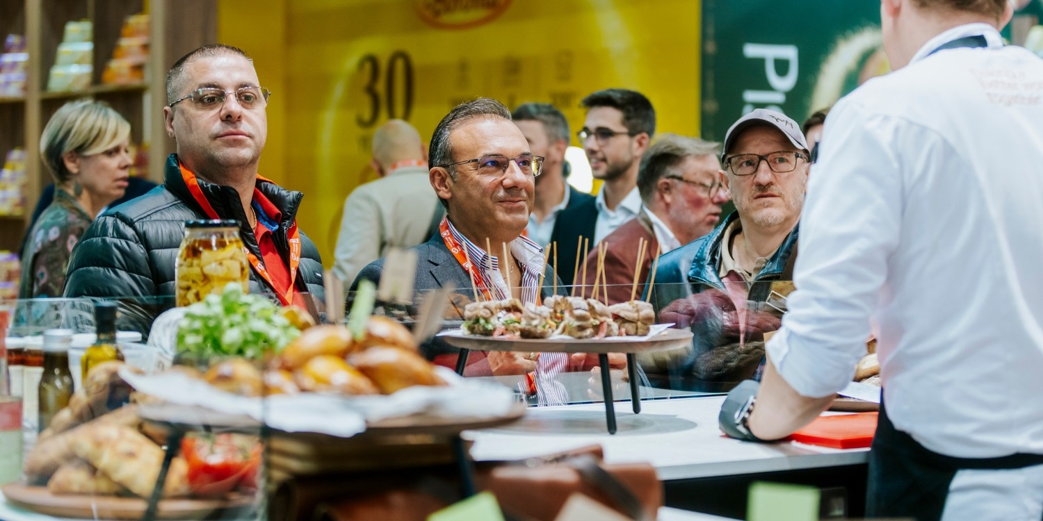 Besucherinnen und Besucher schauen sich einen Messestand mit Kostproben auf der Anuga an. . Artikel "Pflanzliche Vielfalt, Functional Food und Co." öffnen.