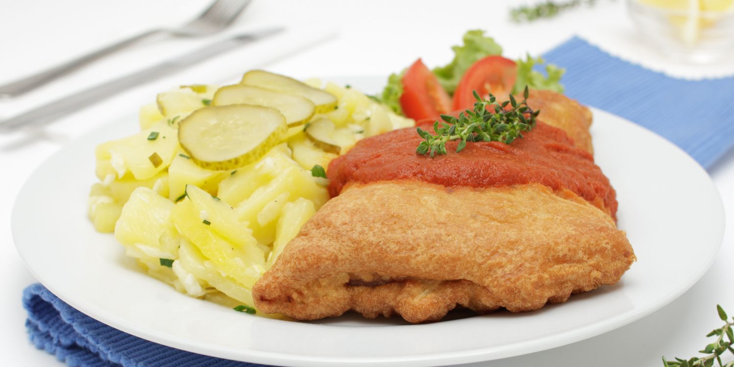 Auf einem weißen Teller liegt ein Stück paniertes Fischfilet mit Tomatensauce, daneben Kartoffelsalat mit Gurkenscheiben. . Artikel "Fisch auf dem Weihnachtstisch" öffnen.