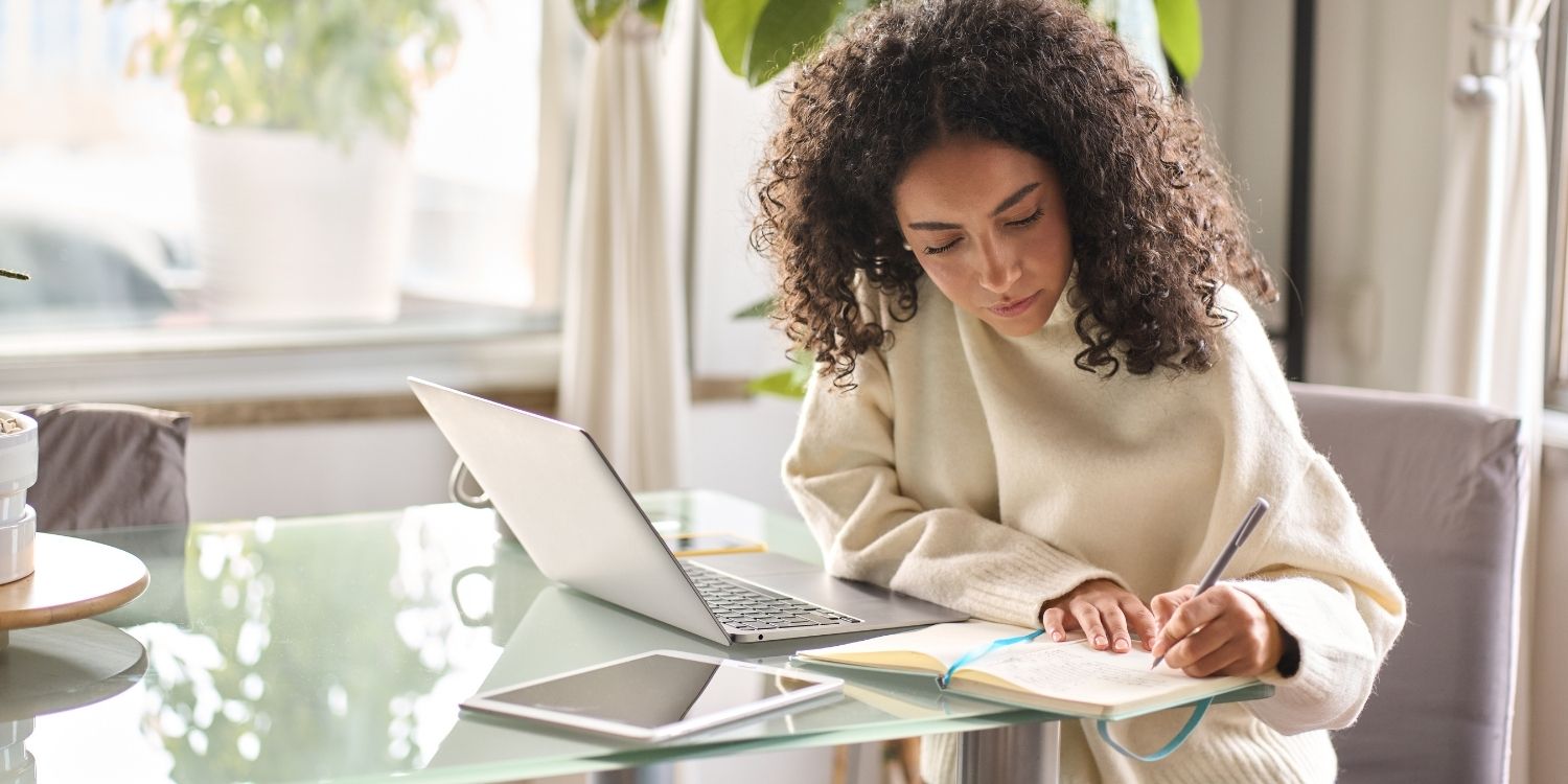 Eine junge Frau sitzt zuhause am Tisch vor ihrem Laptop und macht sich daneben Notizen in ein Heft. . Artikel "Neues Lernportal für Lehrkräfte" öffnen.
