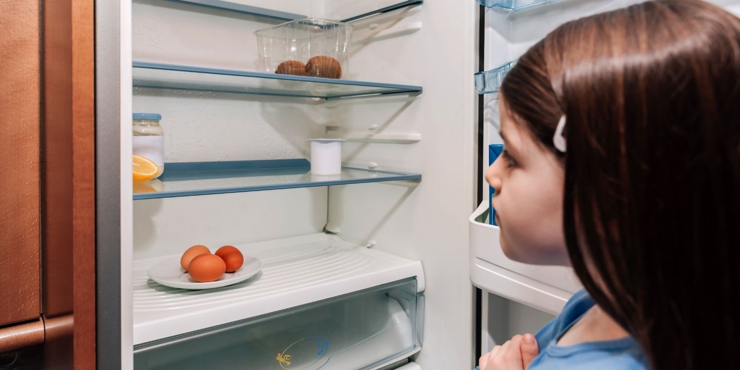 Ein dunkelhaariges Mädchen im Grundschulalter öffnet einen Kühlschrank und schaut sich dessen spärlichen Inhalt an.. Artikel "Ernährungsarmut erkennen und begegnen" öffnen.