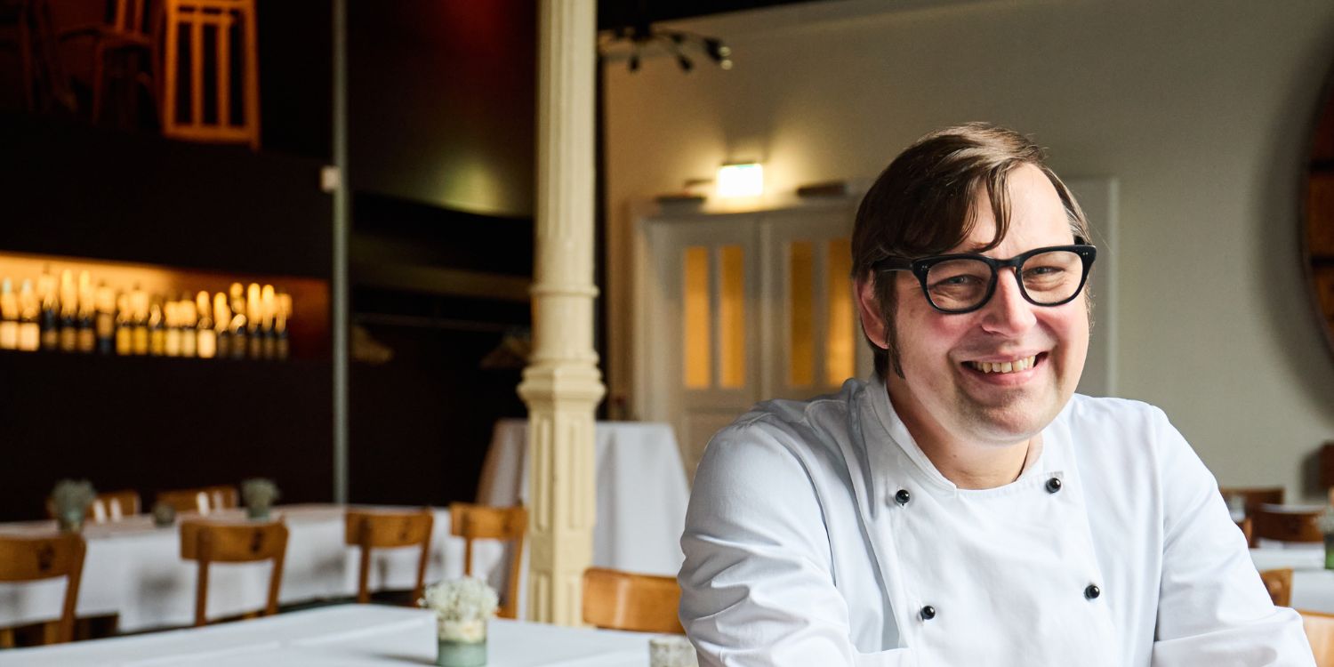 Koch Bernd Ratjen sitzt an einem Tisch im Gastraum seines Gasthofes.. Artikel "#2 Alles auf die Bio-Karte" öffnen.