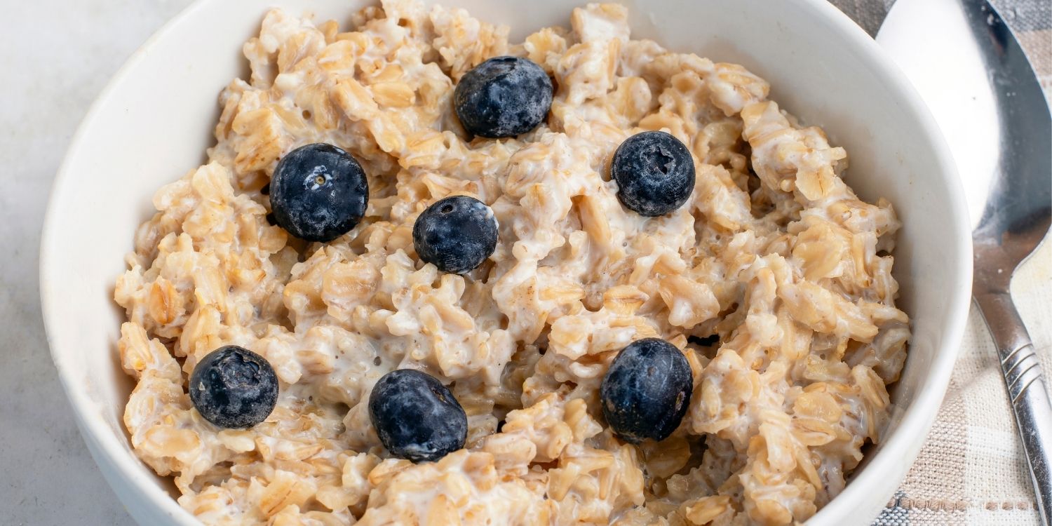 In einer weißen Schüssel sind Haferflocken als Porridge angerichtet und mit Blaubeeren garniert, daneben liegt ein Löffel. . Artikel "Hafer ist glutenhaltig – oder doch nicht?" öffnen.
