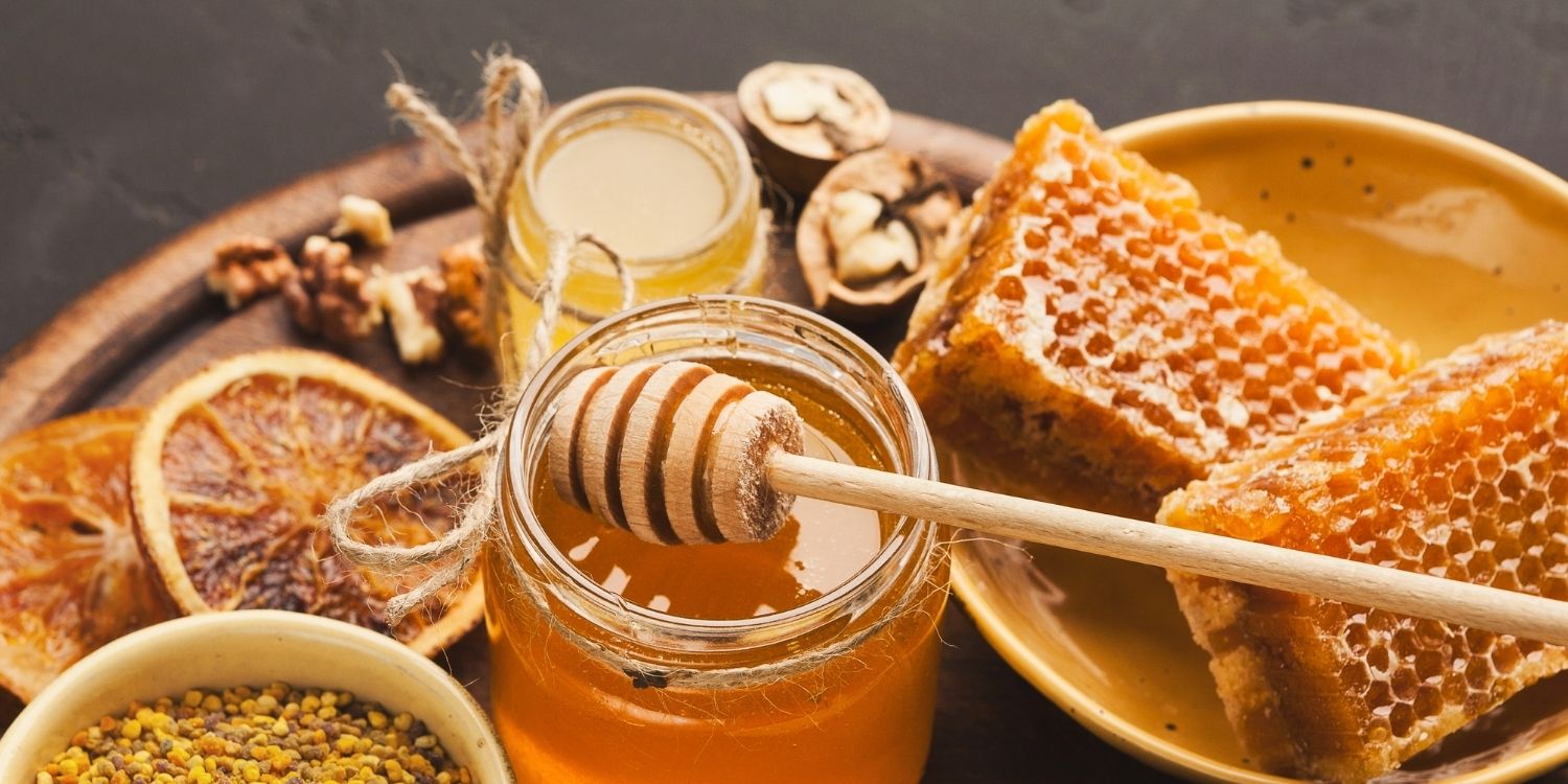 Zwei Gläser Honig auf einem Tablett, daneben steht eine Schale mit Honigwaben und eine mit Pollen. . Artikel "Honig – mehr als nur süß" öffnen.