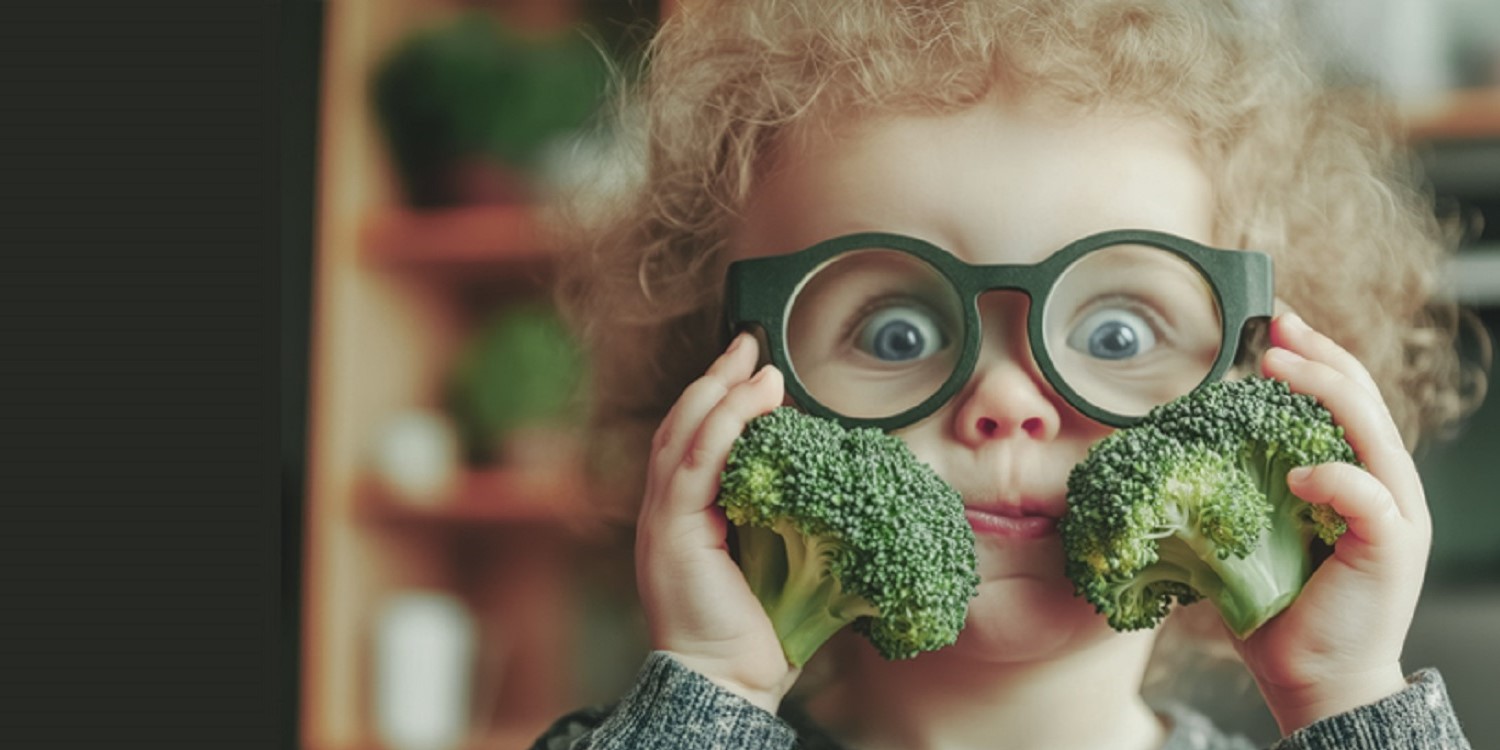 Ein kleiner blonder Junge mit grüner Brille hält zwei Brokkoli-Röschen vor sein Gesicht.. Artikel "Ist Bildung der Schlüssel zu mehr Ernährungskompetenz? " öffnen.