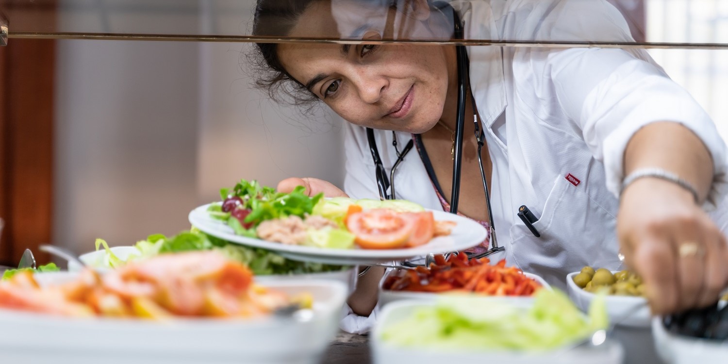 Eine Ärztin steht vor dem Salatbuffet in der Kantine und befüllt ihren Teller mit verschiedenen Salaten. . Artikel "Mehr Nachhaltigkeit in Mensa und Kantine" öffnen.