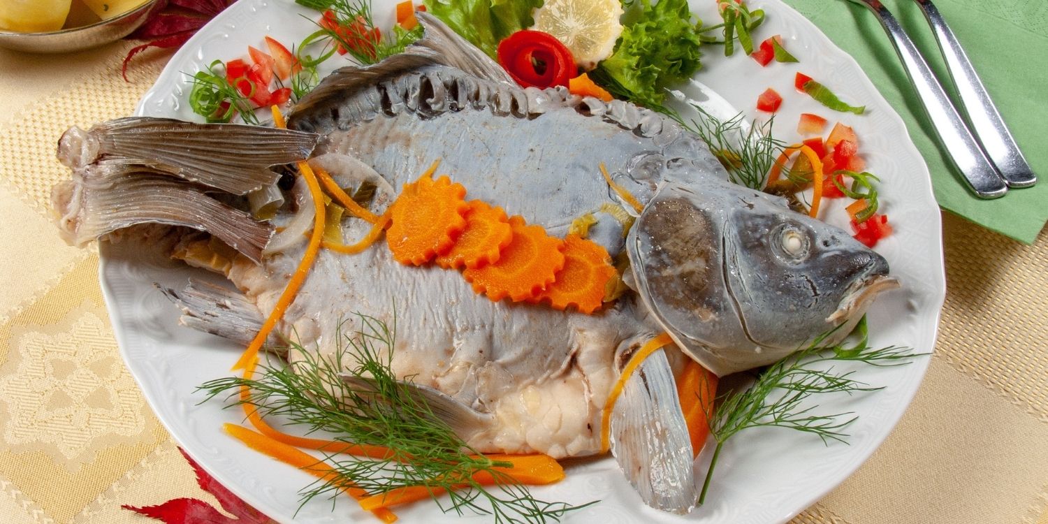 Ein ganzer gegarter Karpfen liegt auf einem Teller, garniert mit Möhren, Dill und Zitrone. . Artikel "Karpfen für die Festtage" öffnen.