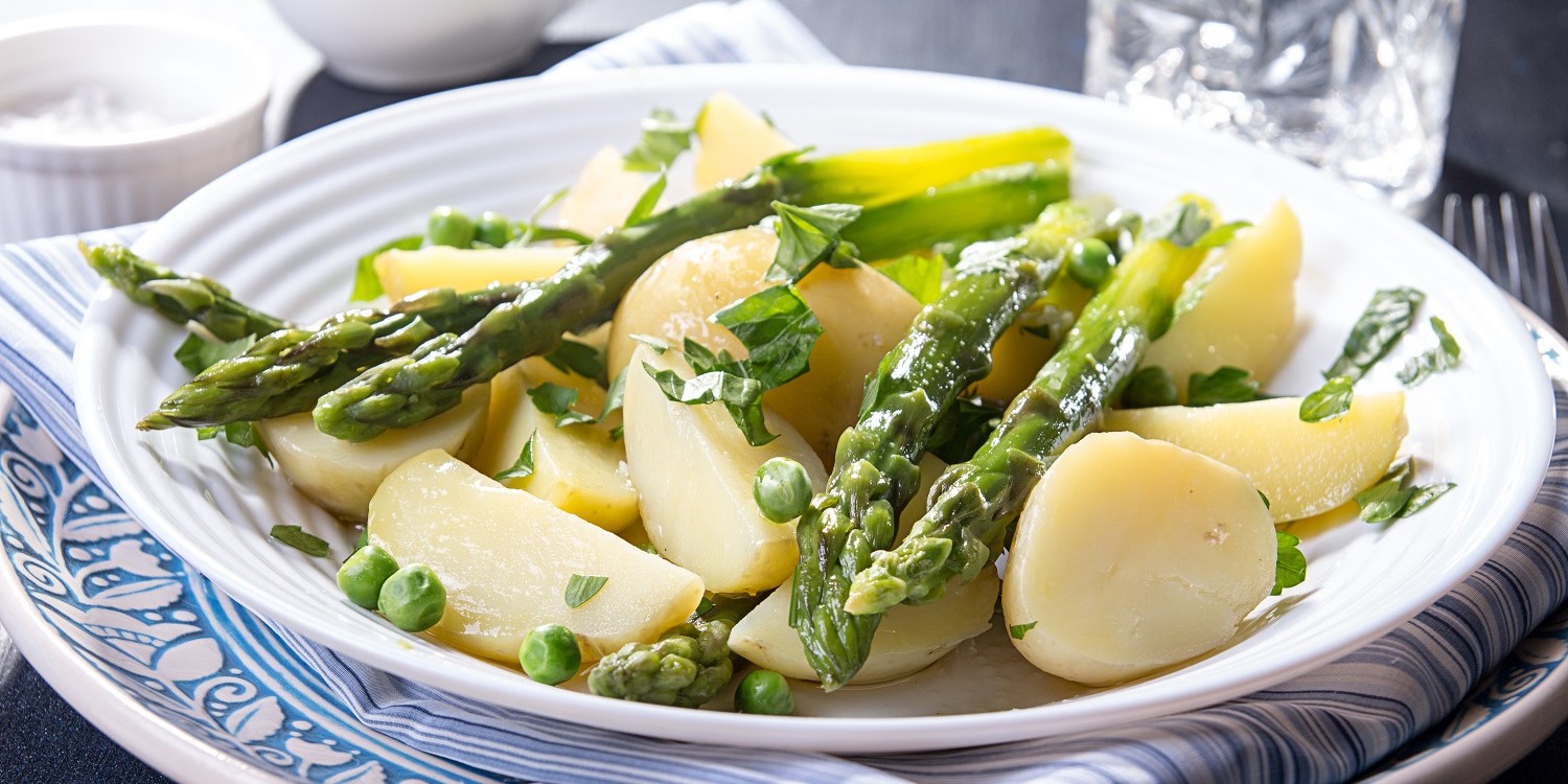 Auf einem weißen Teller liegen gekochte Kartoffeln mit grünem Spargel, Erbsen und Kräutern. . Artikel "Die Frühkartoffel – frisch vom Feld" öffnen.