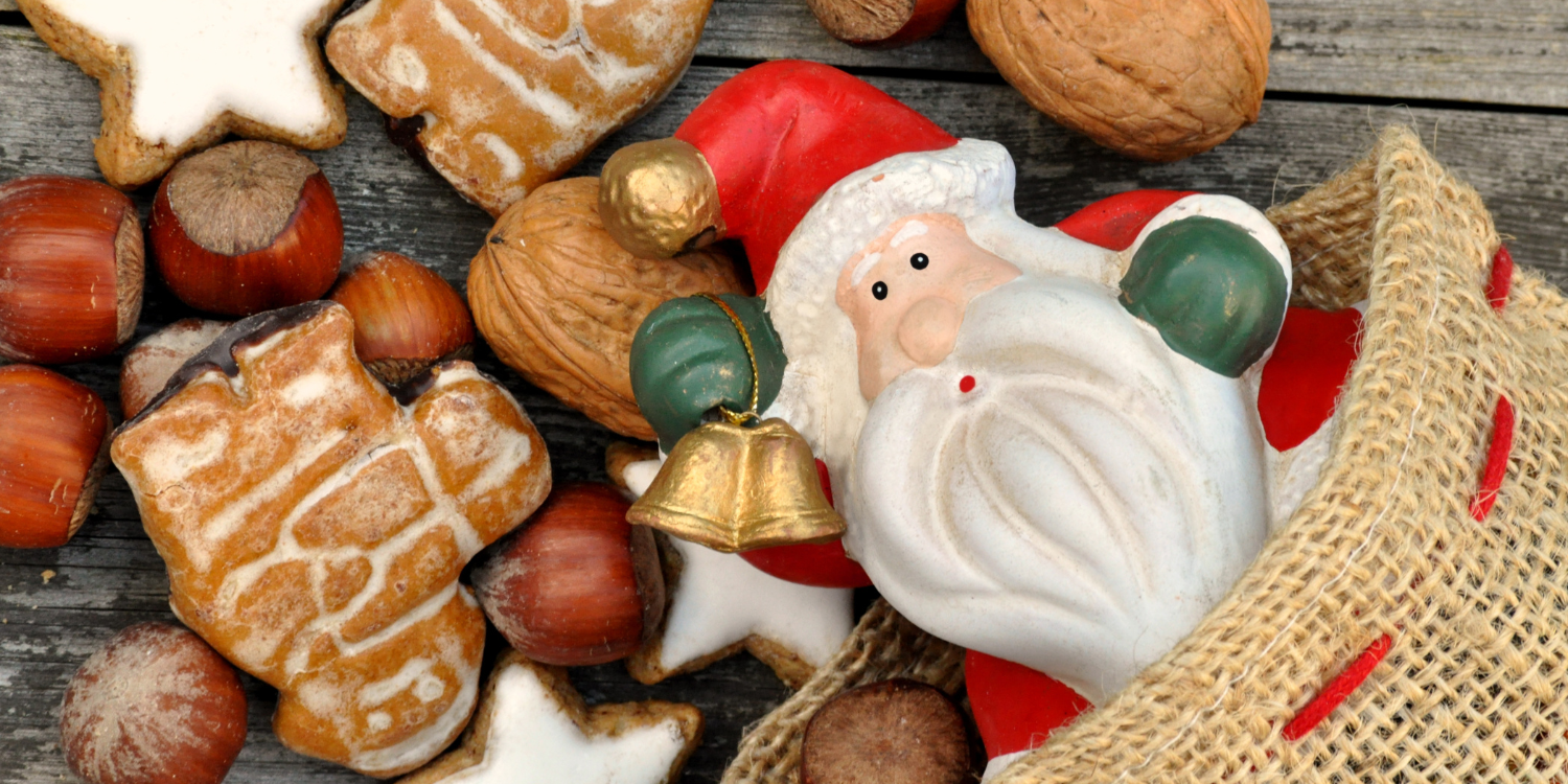 Eine Nikolausfigur schaut aus einem Jutesack hervor. Darum liegen Walnüsse und Haselnüsse sowie Weihnachtsgebäck.  . Artikel "Nikolausstiefel bunt befüllen" öffnen.