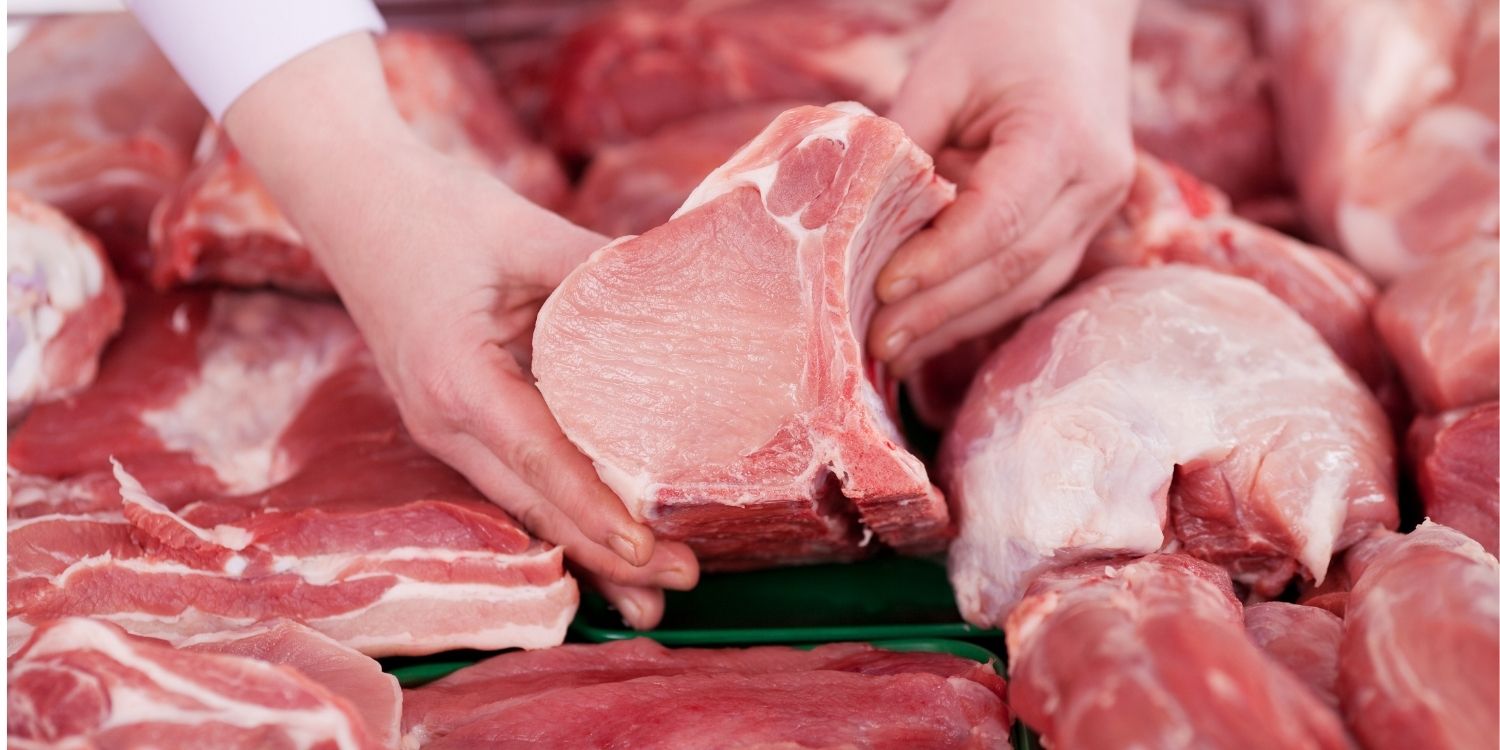 An einer Fleischtheke halten Hände ein Stück Schweinefleisch. . Artikel "Rund ums Schweinefleisch gut informiert" öffnen.