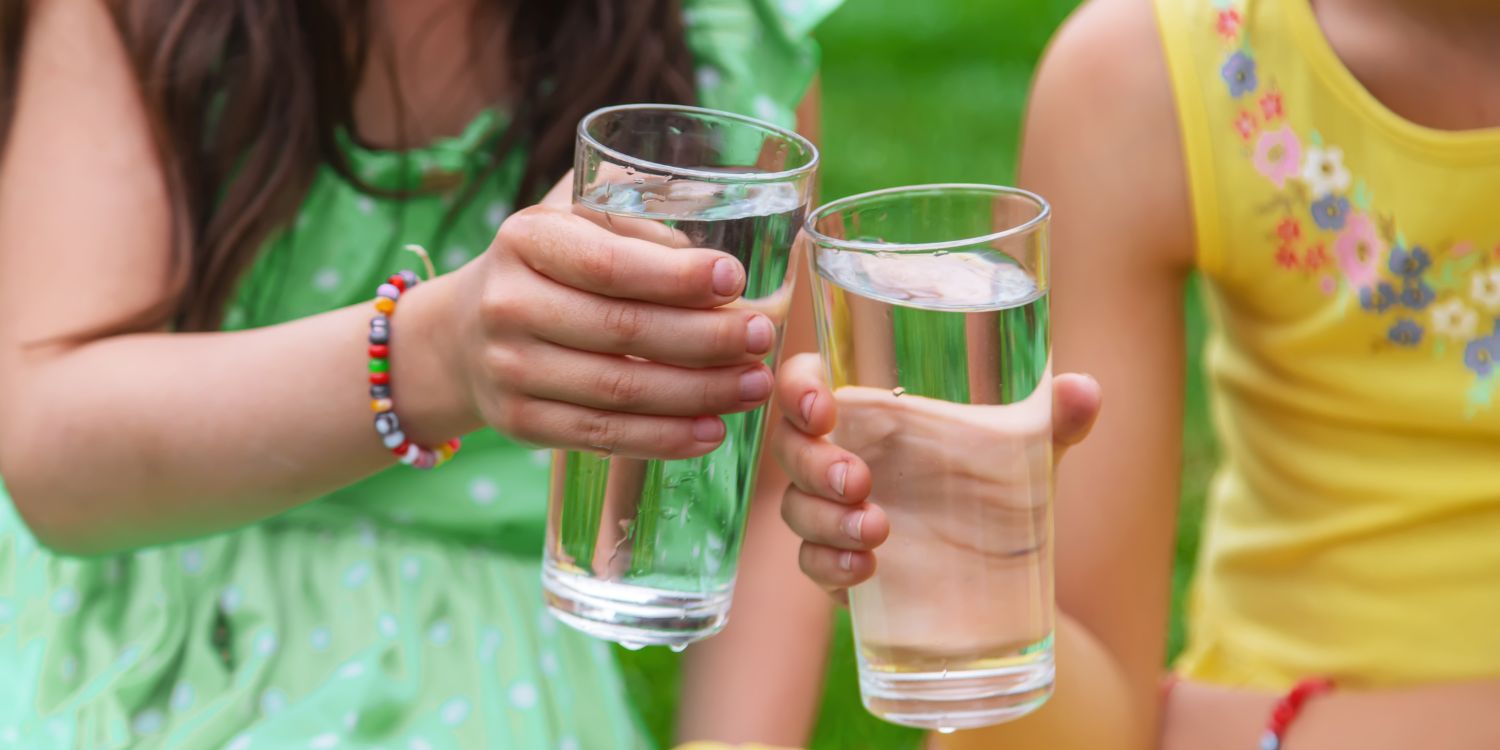 Zwei Mädchen stoßen mit zwei vollen Wassergläsern miteinander an.. Artikel "Was ist das Gegenteil von durstig?" öffnen.