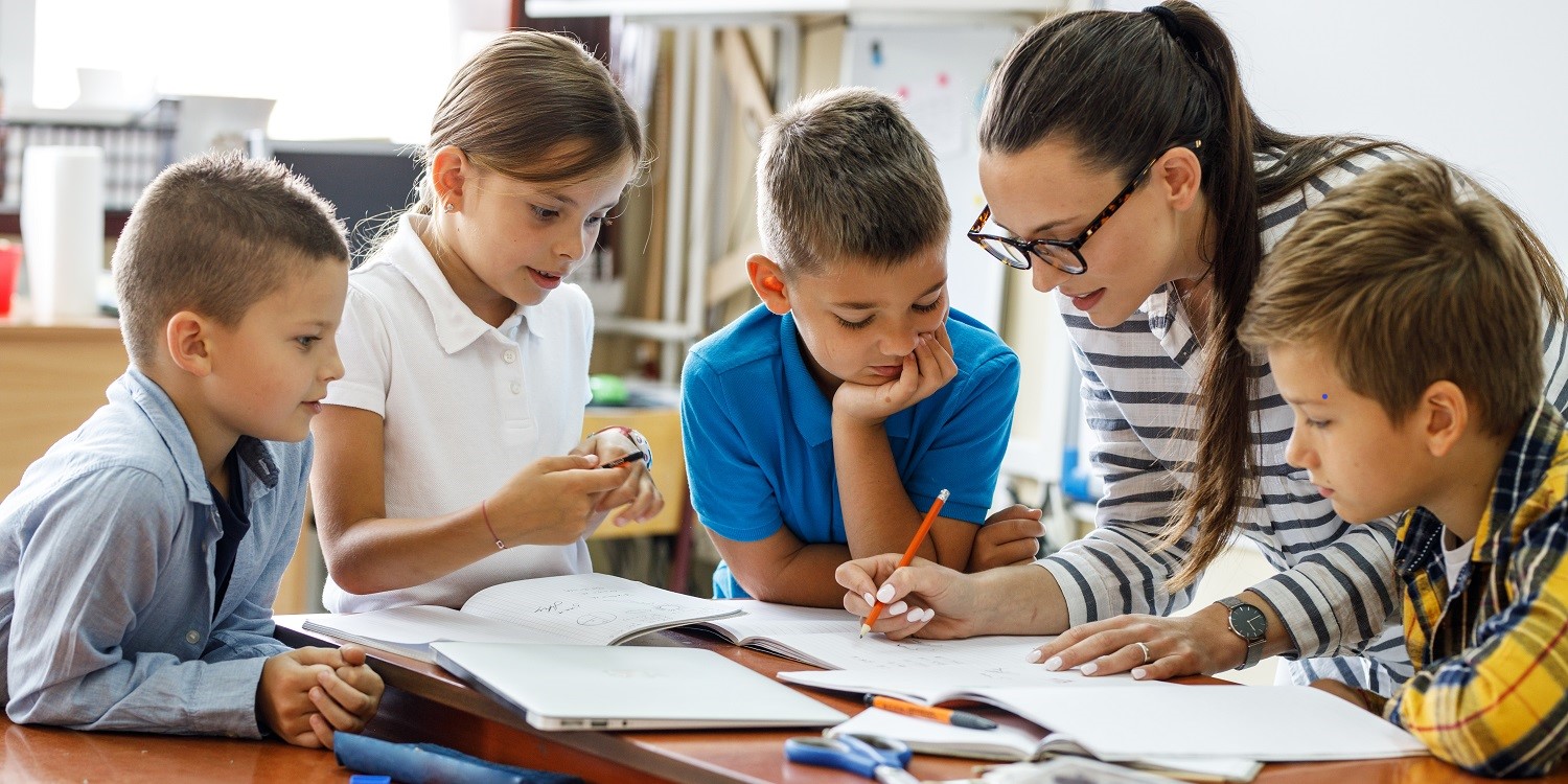Eine Lehrerin, drei Schüler und eine Schülerin sitzen an einem Tisch und arbeiten in einem Unterrichtsmaterial. . Artikel "Wie lassen sich gute Unterrichtsmaterialien erkennen?" öffnen.