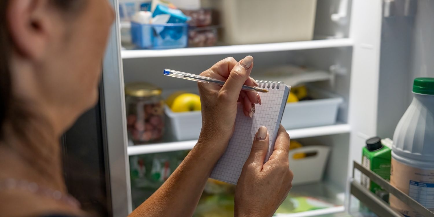 Vor einem geöffneten Kühlschrank steht eine Frau und macht sich Notizen auf einem Einkaufszettel.. Artikel "Aktionswoche „Zu gut für die Tonne!“ 2026" öffnen.