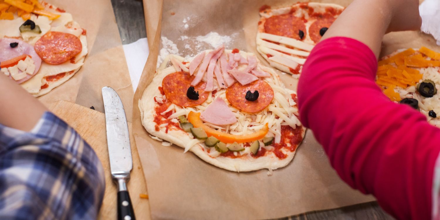 Kinder belegen ausgerollte Teigfladen mit verschiedenen Pizzazutaten und bilden daraus lustige Gesichter. . Artikel "Ernährungsbildung auch im Ganztag" öffnen.
