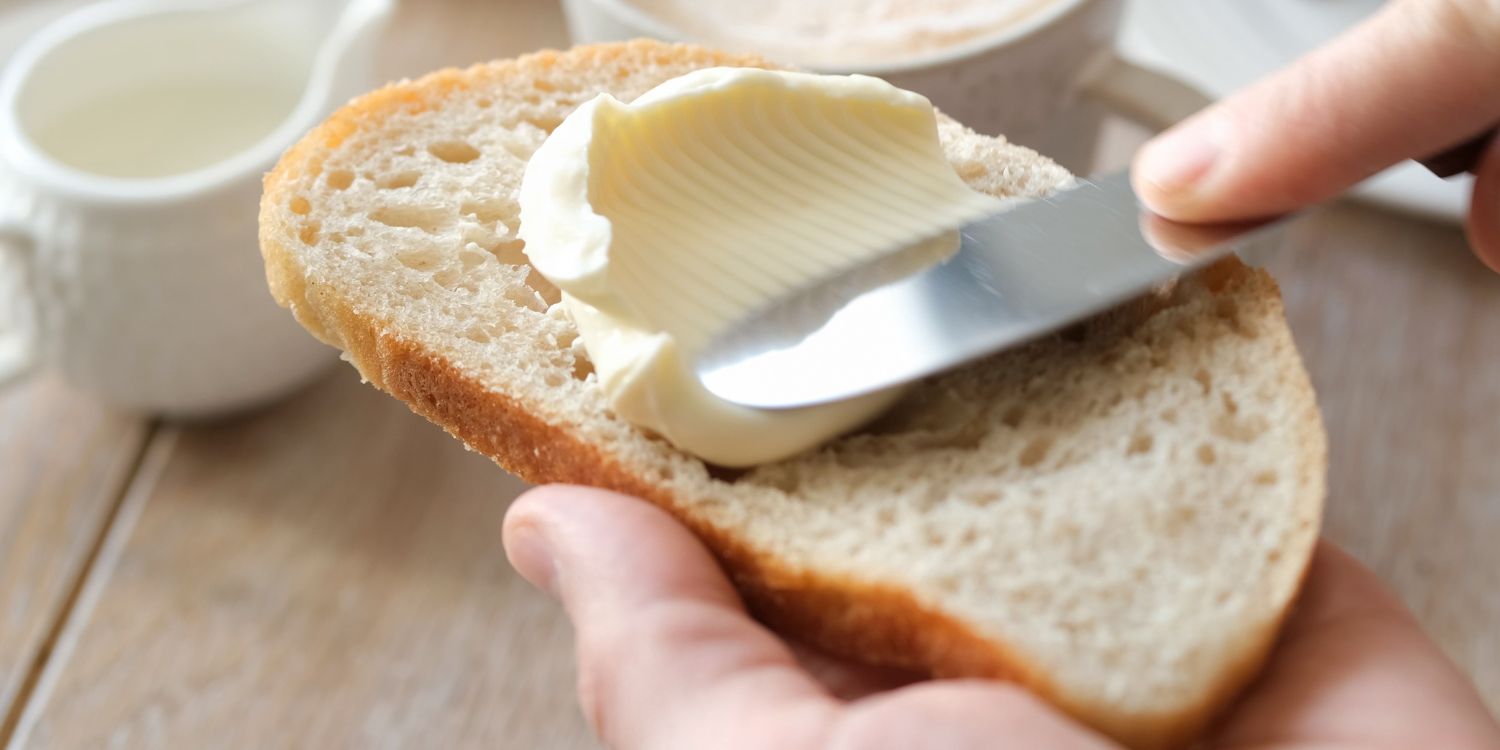 Eine Hand streicht mit einem Messer Butter auf eine Scheibe Brot. . Artikel "Schwankende Butterpreise" öffnen.