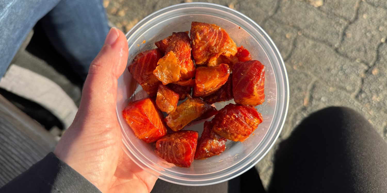 Eine Hand hält eine Plastikschale mit glasierten und geräucherten Lachsstücken darin. . Artikel "Social-Media-Hype: Candy Salmon" öffnen.