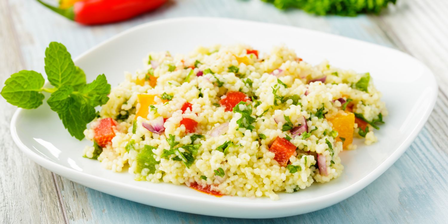 Auf einem weißen Teller befindet sich eine Portion Couscous-Salat mit roter und gelber Paprika, Lauch und Kräutern. . Artikel "Wenn’s schnell gehen muss" öffnen.