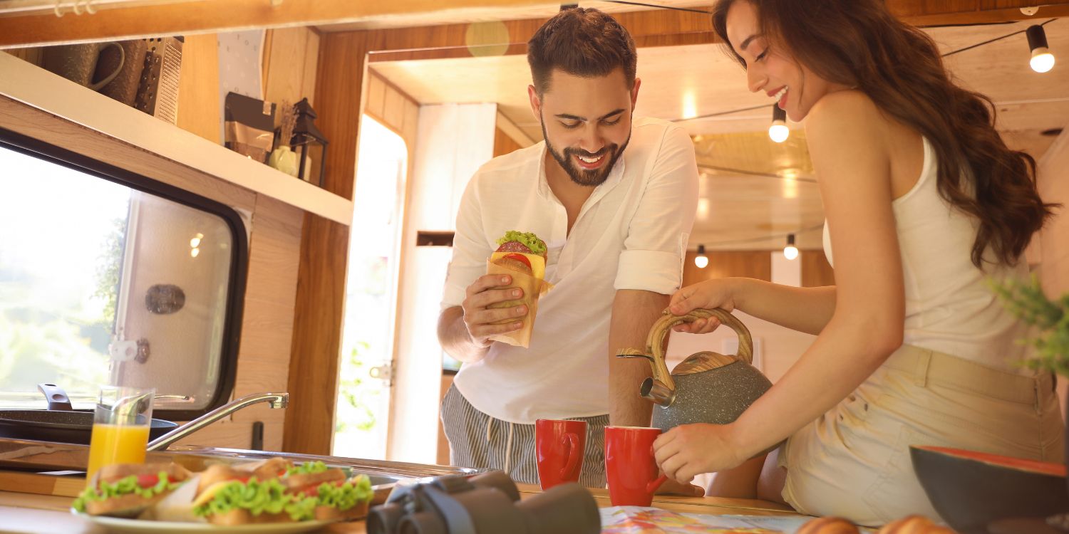 Ein junges Paar frühstückt in einer Ferienwohnung. Es gibt Orangensaft, Kaffee und belegte Brote mit Salat und Tomate. . Artikel "Gut essen in der Ferienwohnung" öffnen.