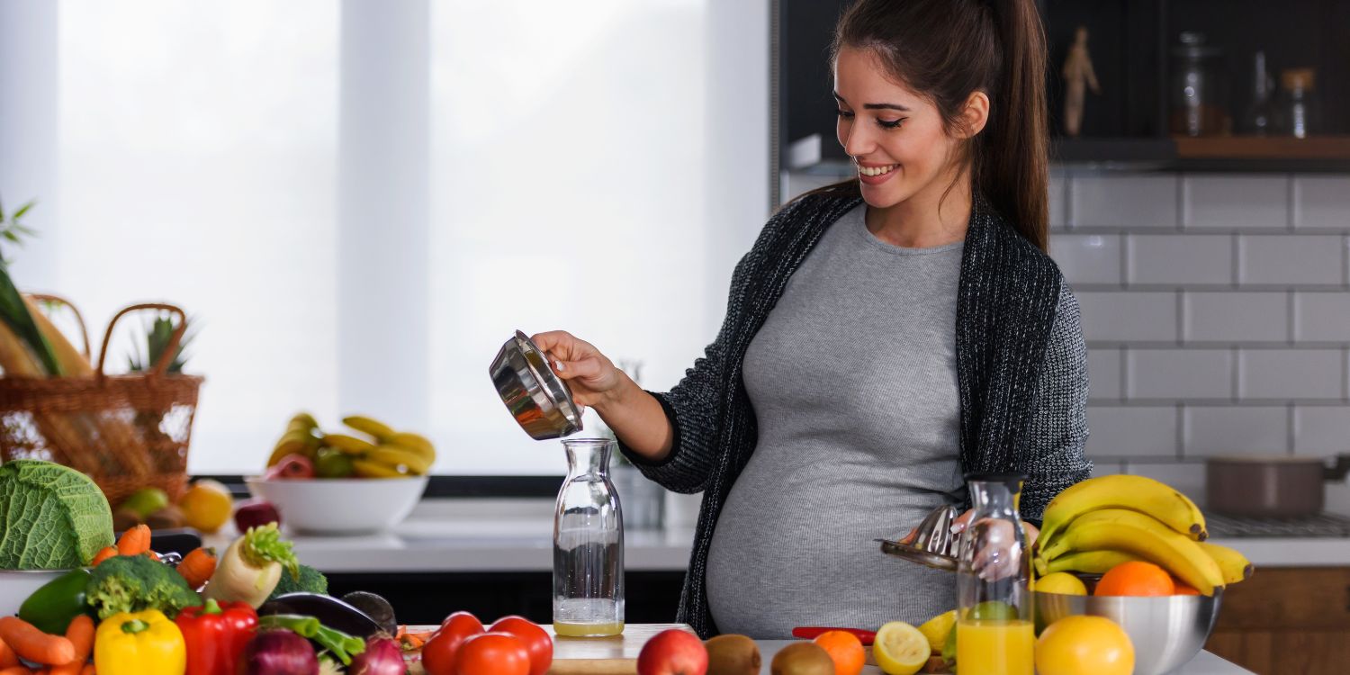 Eine junge dunkelhaarige Schwangere steht in einer Küche und gießt Saft aus einer Zitruspresse in eine Flasche. Vor ihr auf dem Tresen liegen verschiedene Obst- und Gemüsearten.. Artikel "Presse-Einladung zum Fachtag „Schwangere begleiten“" öffnen.