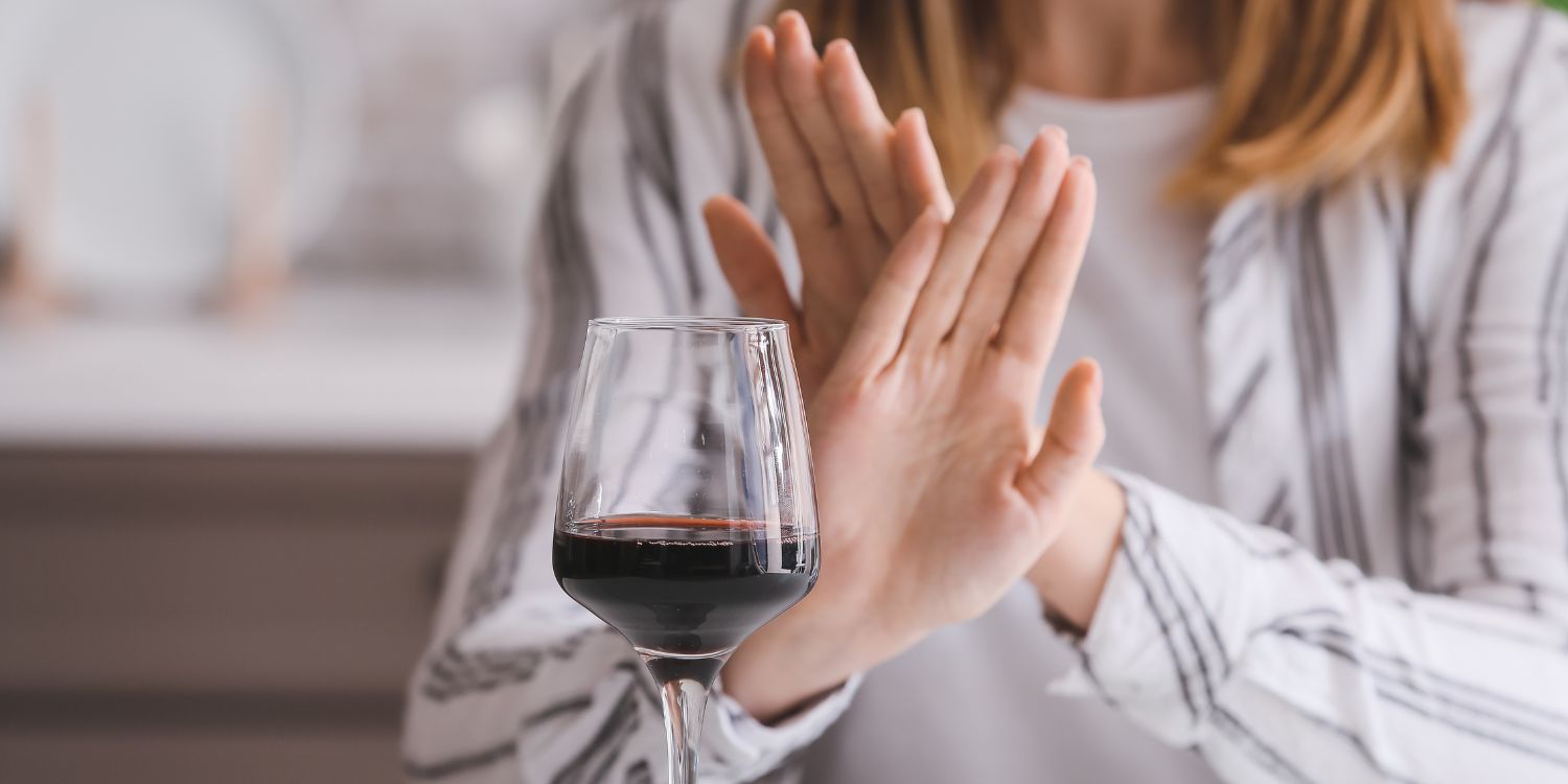 Auf einem Tisch steht ein Glas Rotwein. Eine Frau sitzt davor und macht mit den Händen eine abwehrende Geste.. Artikel "Fasten von Alkohol, Süßigkeiten und Fleisch beliebt" öffnen.