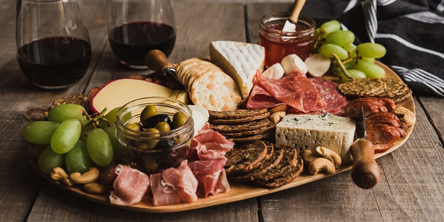 Auf einer ovalen Platte sind verschiedene Käsesorten, Schinken und Wurst mit Trauben, Nüssen, Chutney und Crackern angerichtet.. Artikel "Herbstliche Foodboards" öffnen.
