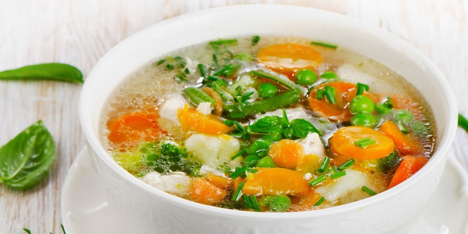 In einer weißen Suppenschale ist klare Suppe mit Möhren, Erbsen; Blumenkohl, Bohnen und Kräutern.. Artikel "Suppenküche im Frühling" öffnen.