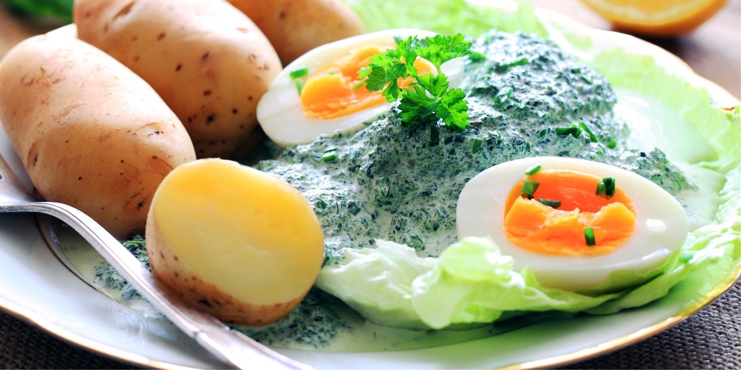 Auf einem weißen Teller sind Pellkartoffeln, hartgekochte Eier mit grüner Soße und Salatblätter angerichtet.. Artikel "Frankfurter Grüne Soße" öffnen.