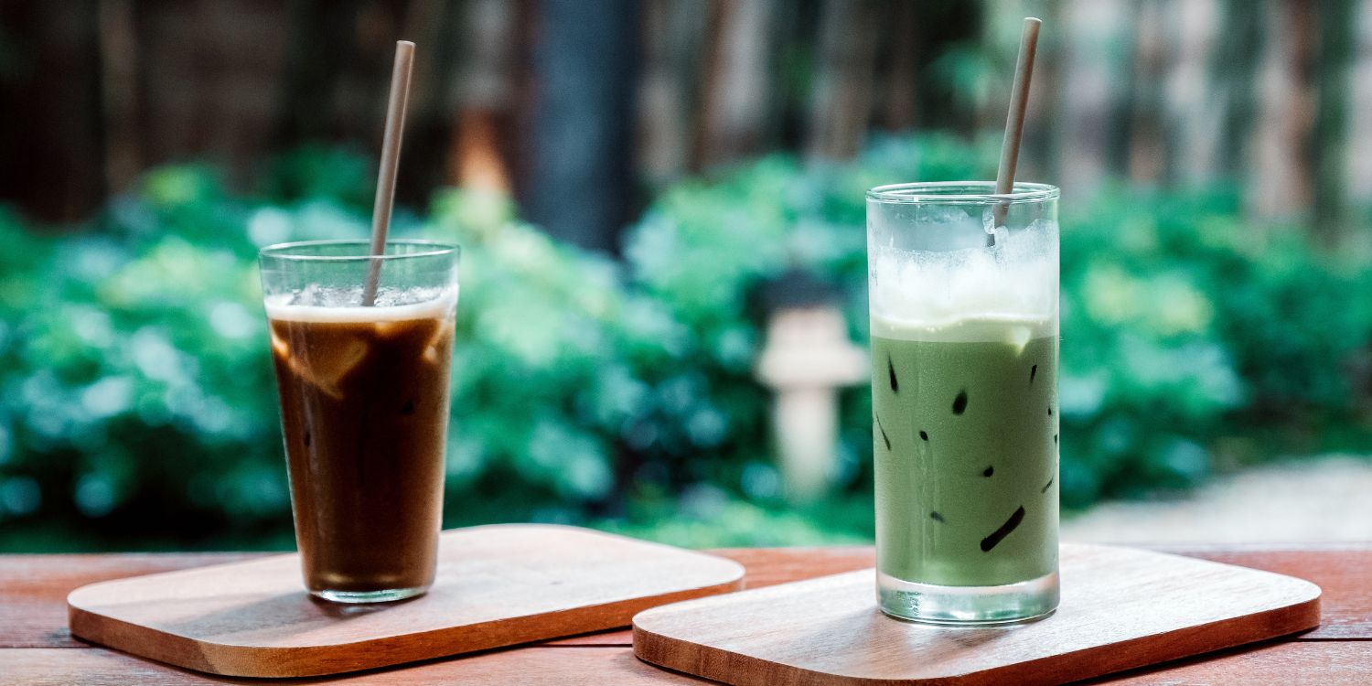 Ein Glas mit Hojicha-Eistee und ein Glas Iced Matcha-Latte stehen nebeneinander auf einem Holztisch.. Artikel "Grüntee: Hojicha und Matcha " öffnen.