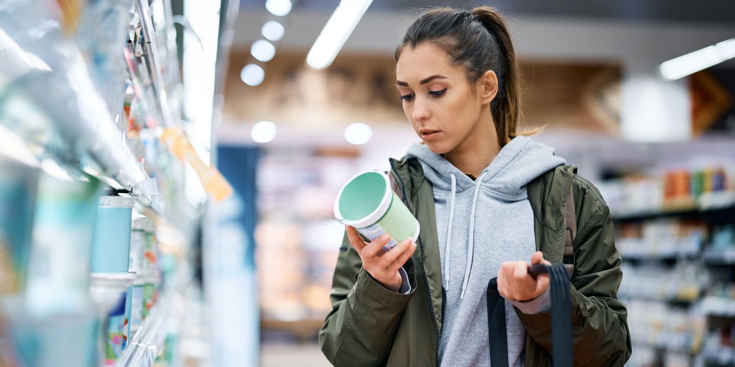 Eine junge Frau liest beim Kauf eines Milchprodukts im Supermarkt das Produktetikett.. Artikel "Werbung mit Umweltfreundlichkeit wird strenger" öffnen.