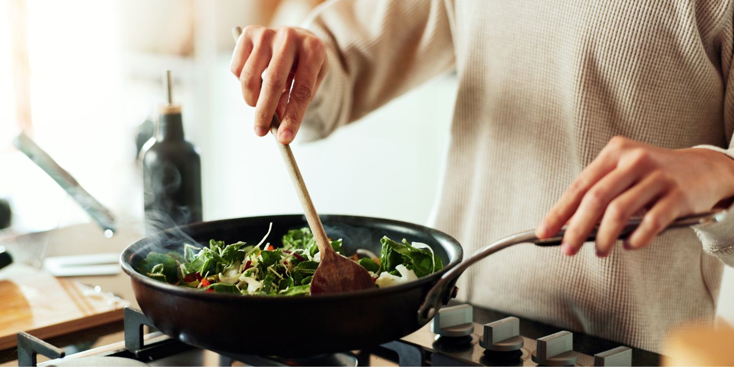 Ein Mann brät in einer Pfanne auf einem Gasherd Gemüse an. Er rührt dabei mit einem Holzlöffel in der Pfanne. . Artikel "Lecker, gesund und restlos glücklich" öffnen.