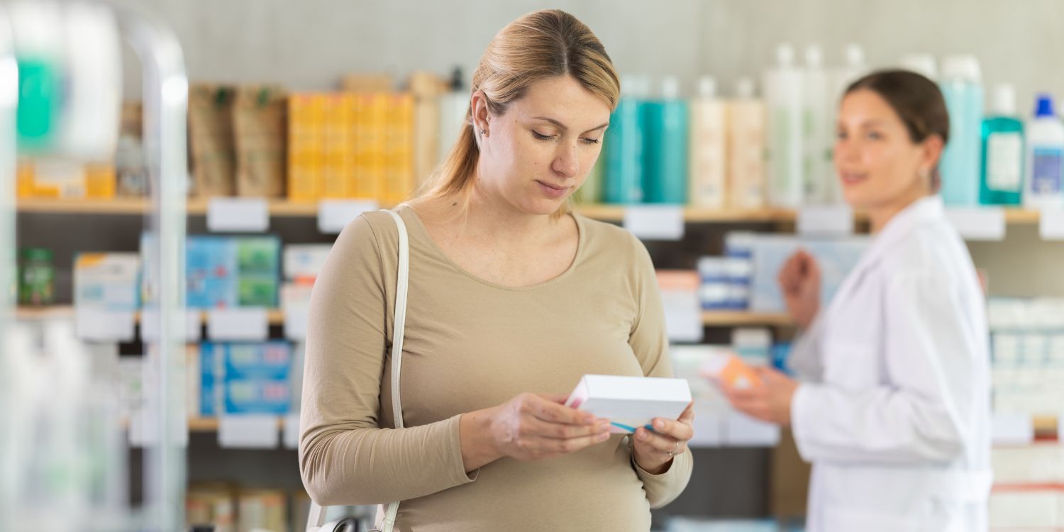 Eine Schwangere steht in der Apotheke und schaut sich eine Verpackung an. . Artikel "Jodversorgung in Deutschland geht zurück" öffnen.