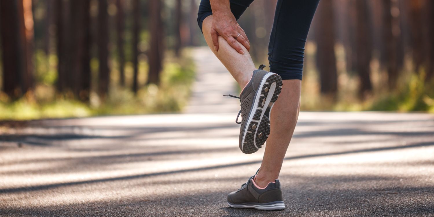 Eine Joggerin auf einem Waldweg hält ihre Wade mit der Hand. . Artikel "Magnesium gegen Muskelkrämpfe" öffnen.