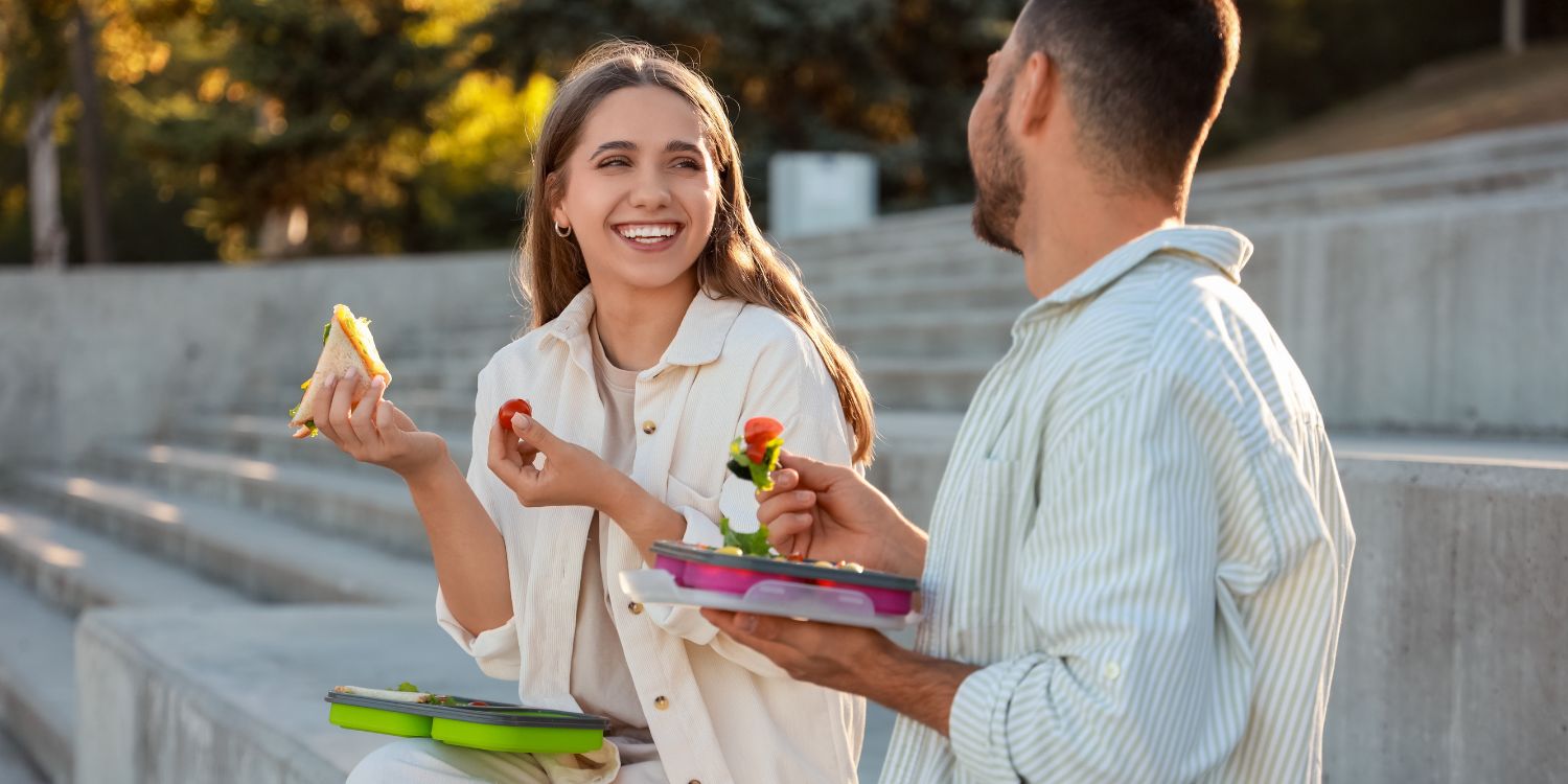 Eine junge Frau und ein junger Mann essen ihr Mittagessen im Freien. . Artikel "Gesundheit im Betrieb fördern" öffnen.