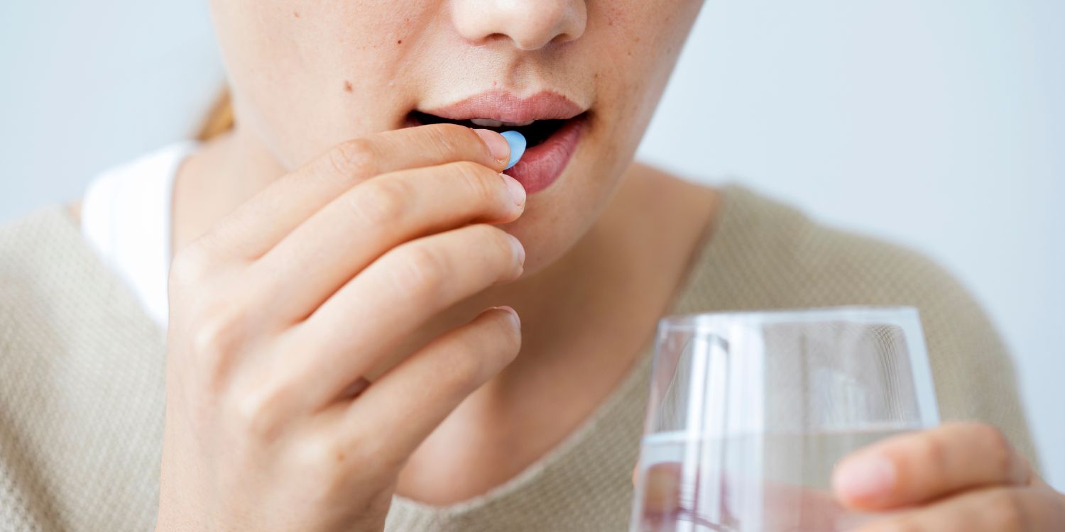 Eine junge Frau steckt eine Tablette in den Mund und hält ein Glas Wasser in der anderen Hand.. Artikel "Brauchen Frauen Extra-Nährstoffe?" öffnen.